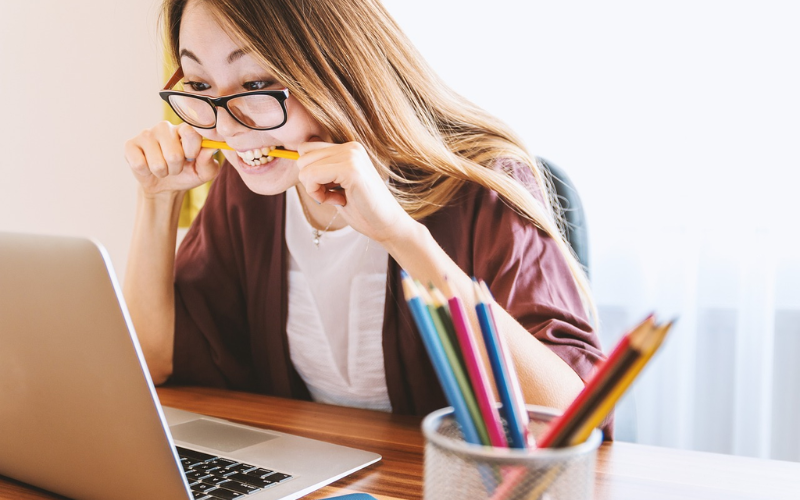 Woman biting a pencil while looking at laptop