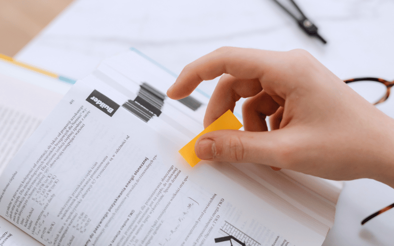 Close-up of a person putting a sticky note on a textbook page 