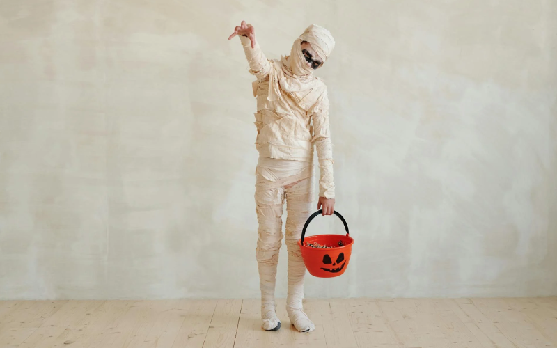 person dressed as mummy holding a bucket with pumpkin design