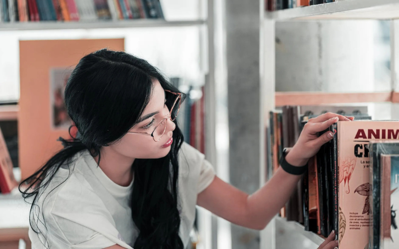 A girl with glasses looking for a book on a shelf