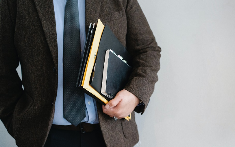 person wearing a suit holding a book and documents