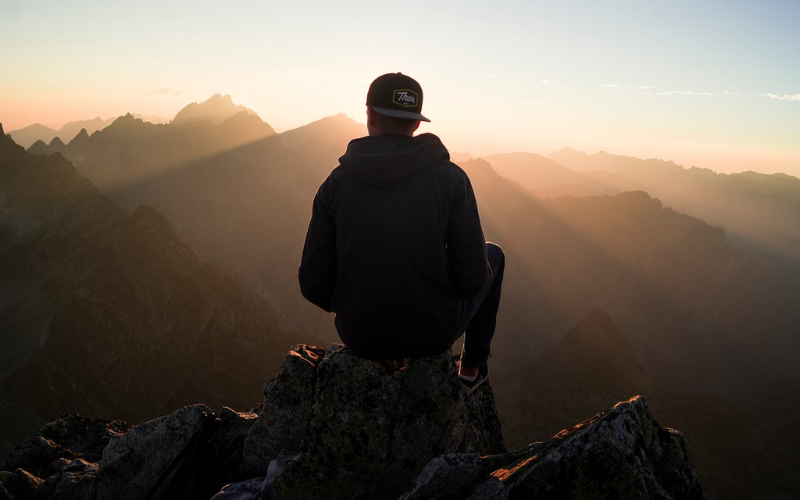 person sitting on a rock on a mountain looking at the horizon