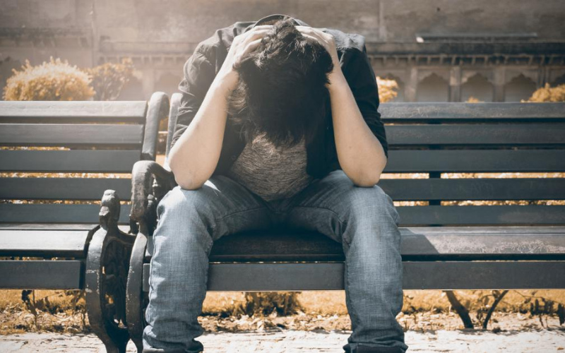 guy on bench with hands at neck and head looking down