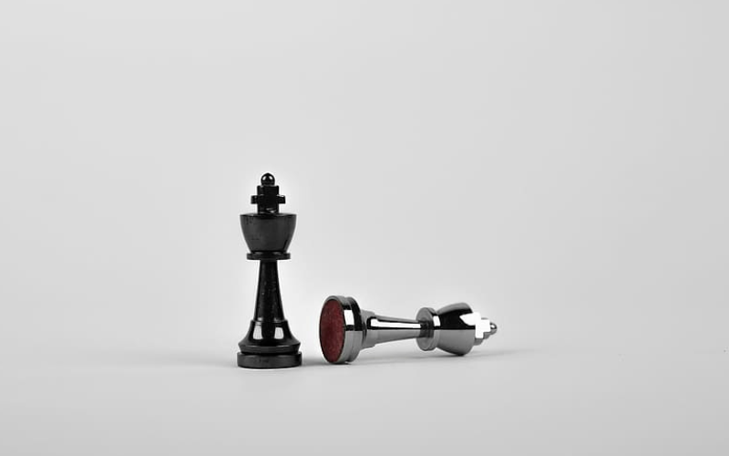 black chess piece standing and silver chess piece fallen over