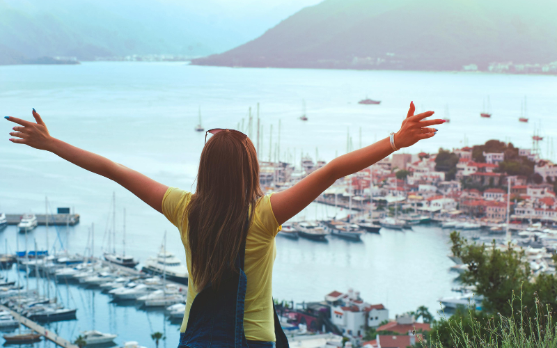 Woman Raising Her Hands Facing Cityscape Near Body of Water