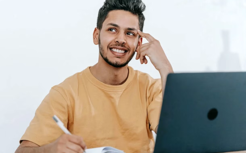 man thinking and working on a book in front of a laptop