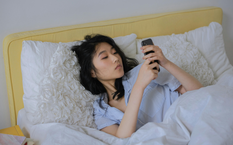 A woman using her smartphone while lying down on the bed