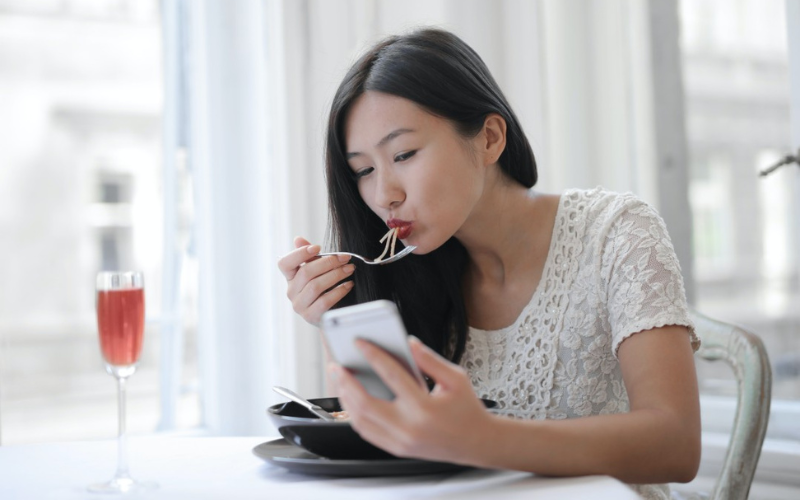 A woman eating while looking at her smartphone