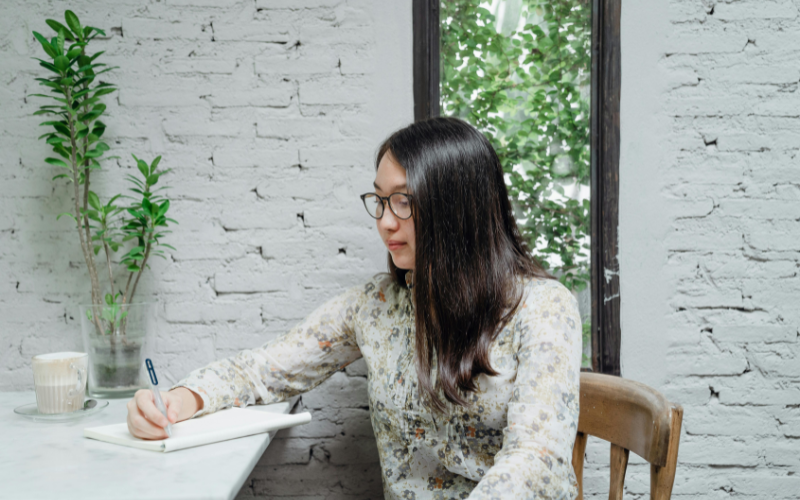 A ladt wearing glasses writing something on a notebook