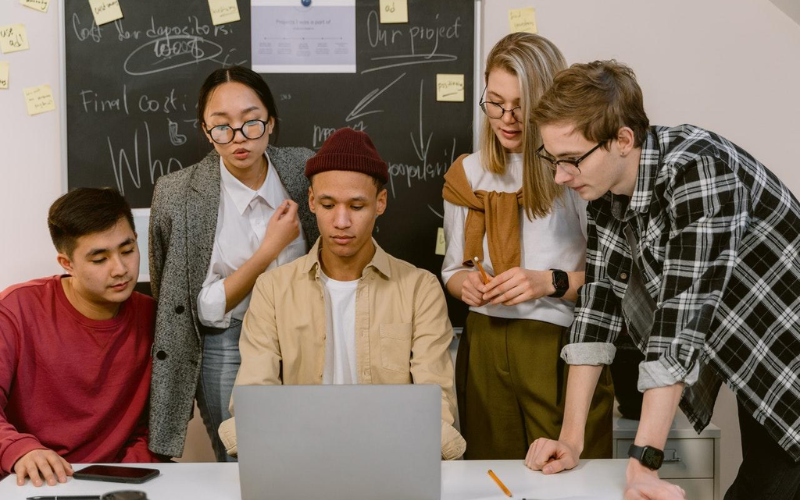 Man looking at laptop with people overlooking