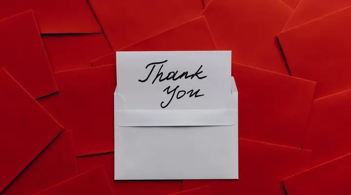 A thank you note written on a white envelope and surrounded by red envelopes