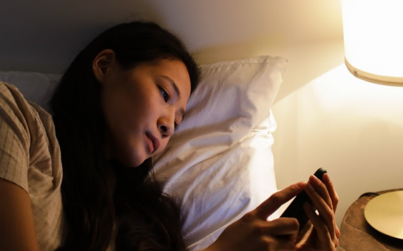 The girl lies in bed an looks at the phone