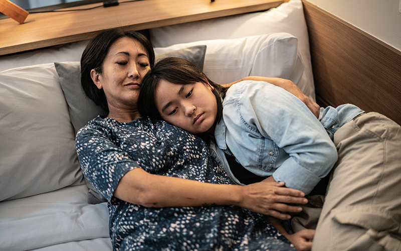 Teenage girl lying on top of her mum seeking comfort
