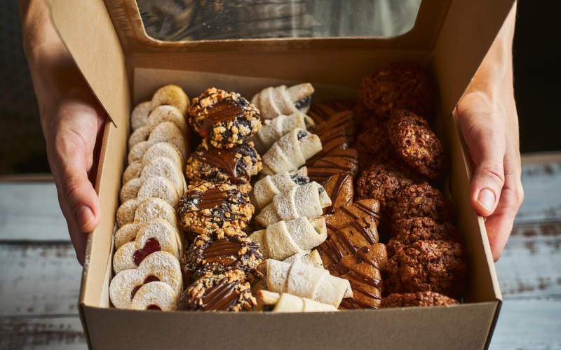 Hands presenting a box of Christmas cookies