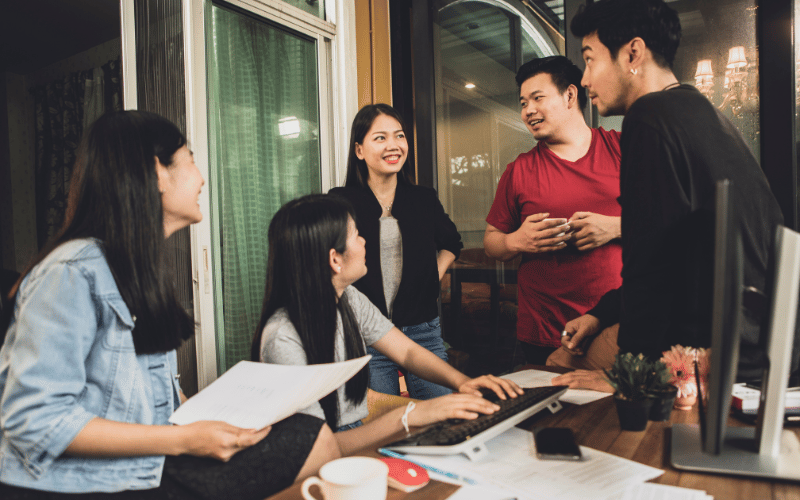 group of young asian adults gather in front of a work desk 