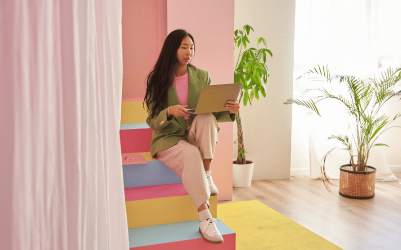 Fashionable lady is working with her laptop by the colourful staircase