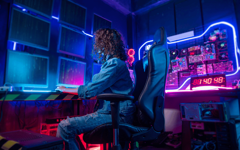 Lady in her dark working room looking at multiple screens showing strings of codes