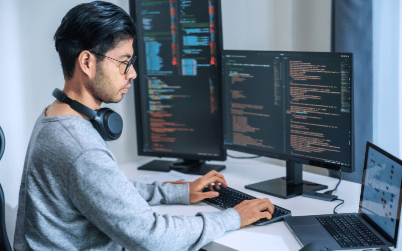  Man working on his coding with multiple desktop screens