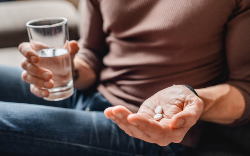 Person holding two aspirin tablets in one hand and a glass of water in another