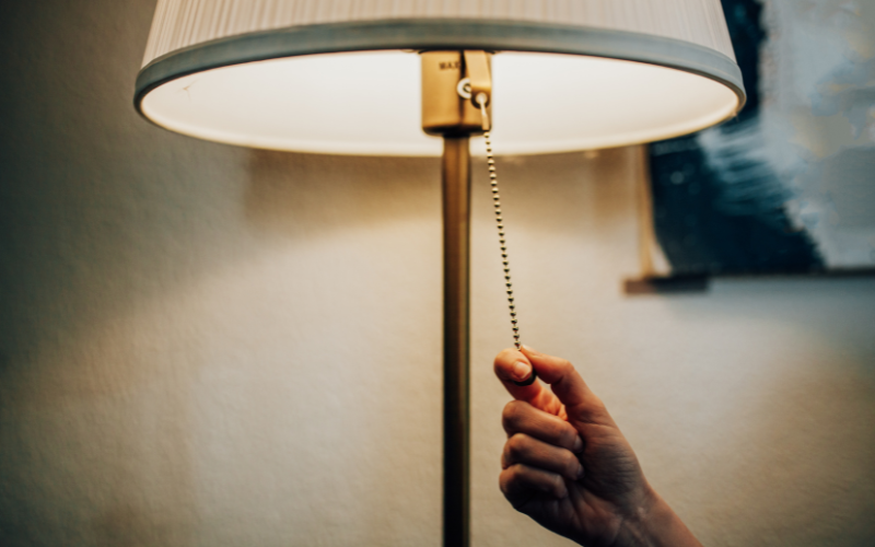 Hand tugging at lamp's pull chain to switch it off