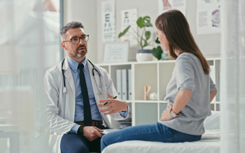 Male doctor speaking to a female patient while she holds her abdomen