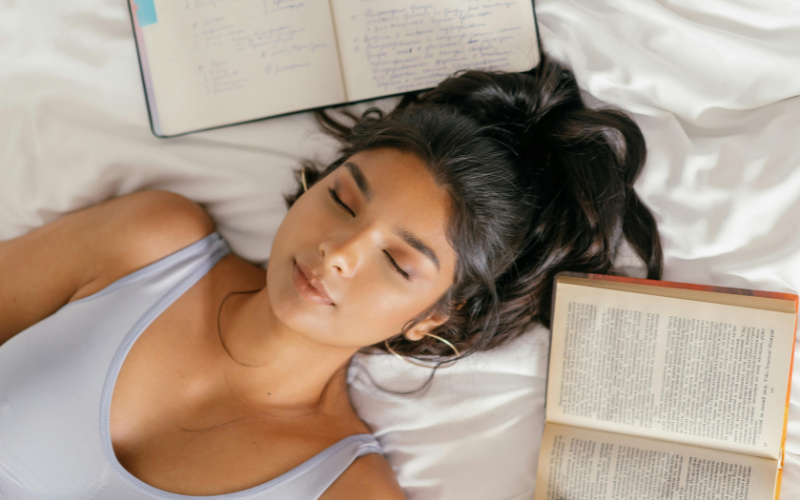 Girl lying in bed with an open journal and book on either side