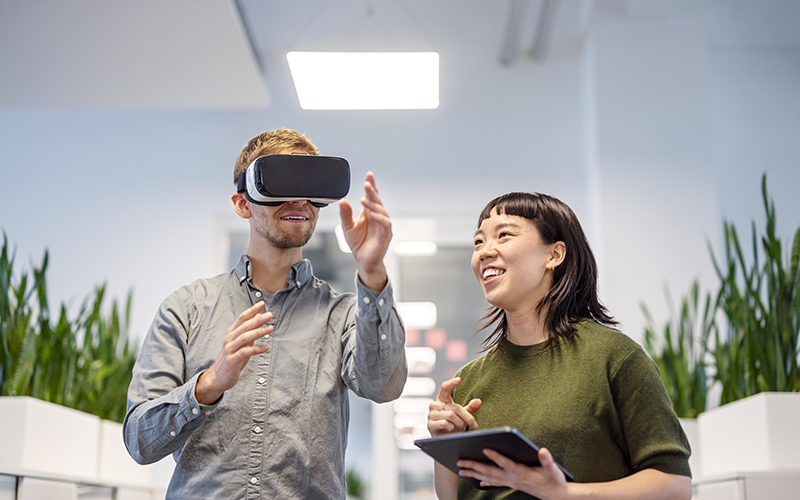 Young man using VR glasses with female colleague holding digital tablet at office