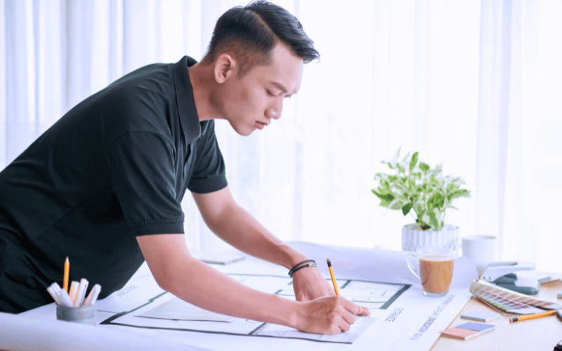 Male student sketching on architectural plans at a desk, symbolising academic pathways in surveying and heritage management.