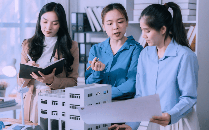 Three students examining a building model and design plans together, illustrating collaborative learning in architecture and built heritage studies