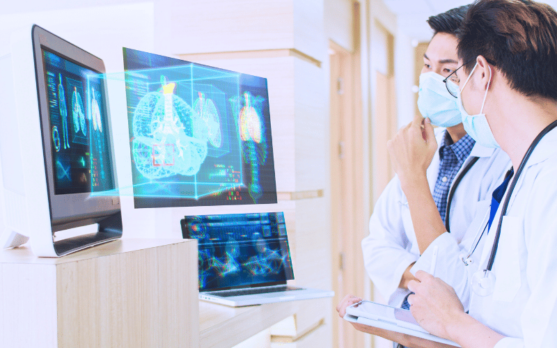 Medical professionals analysing 3D diagnostic scans on digital monitors in a hospital corridor.