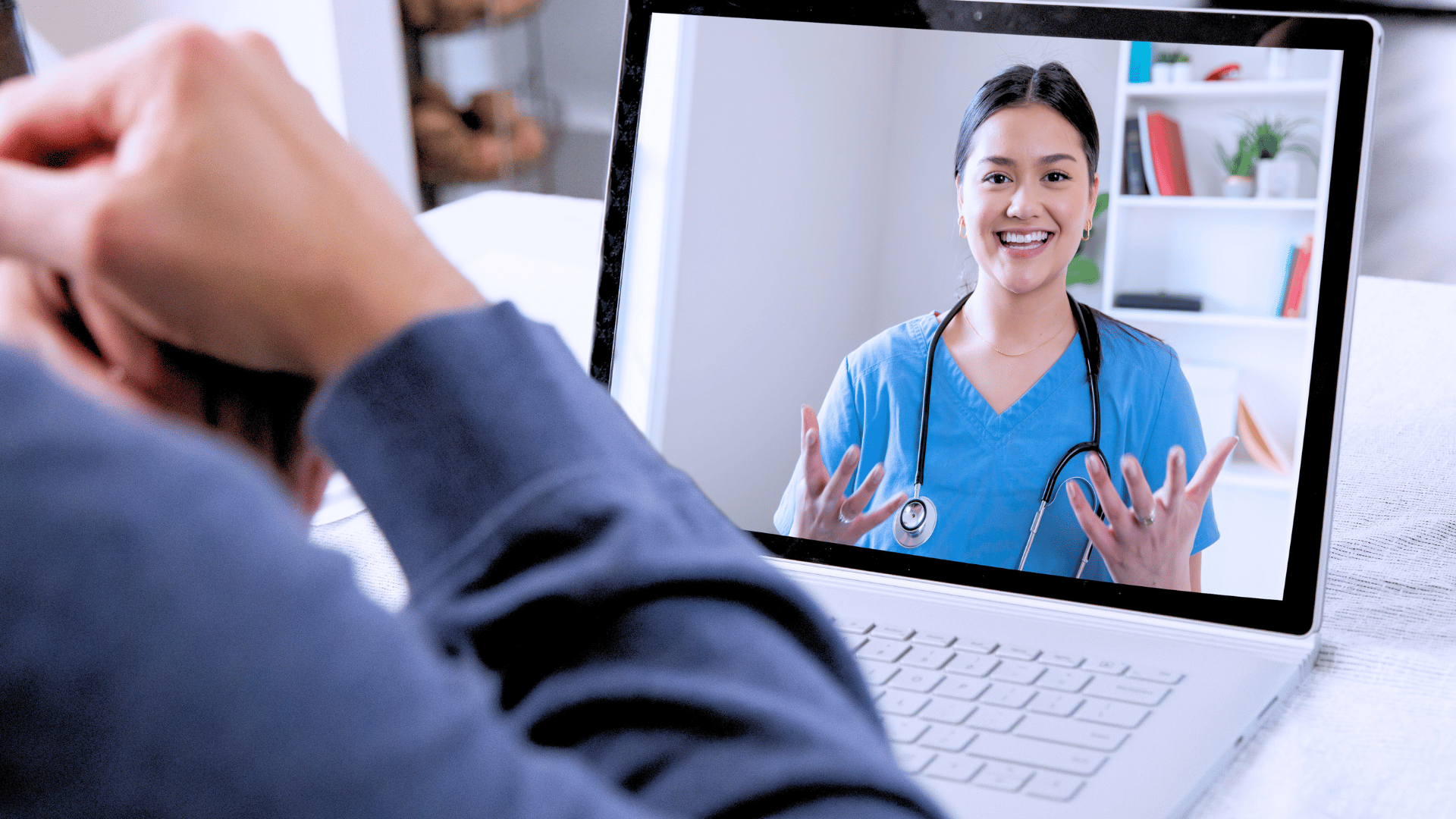 Smiling healthcare professional conducting a virtual consultation on a laptop screen, speaking to a patient remotely.
