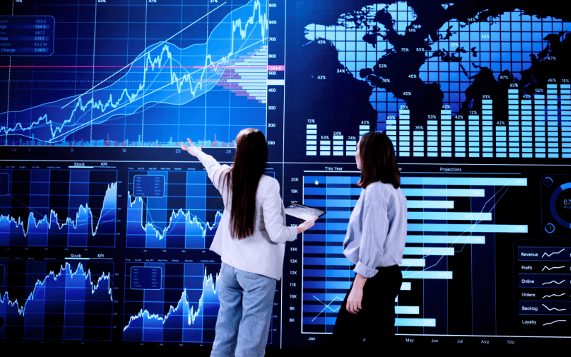 Two female co-workers analysing multiple data on a giant data dashboard display