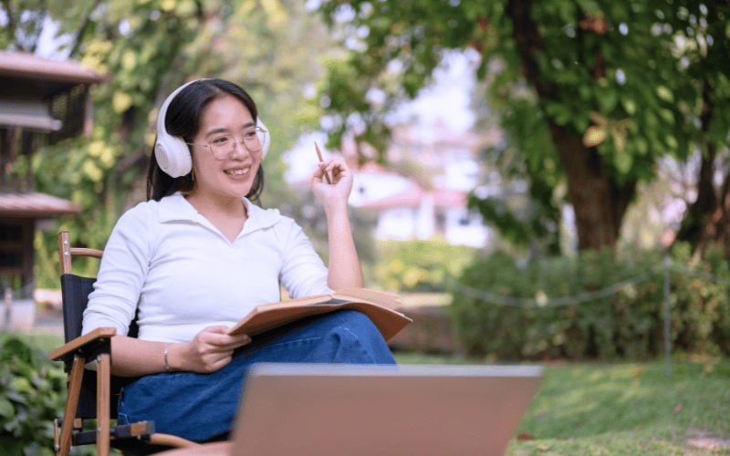 Girl is listening to audio via headphone while writing in the outdoor