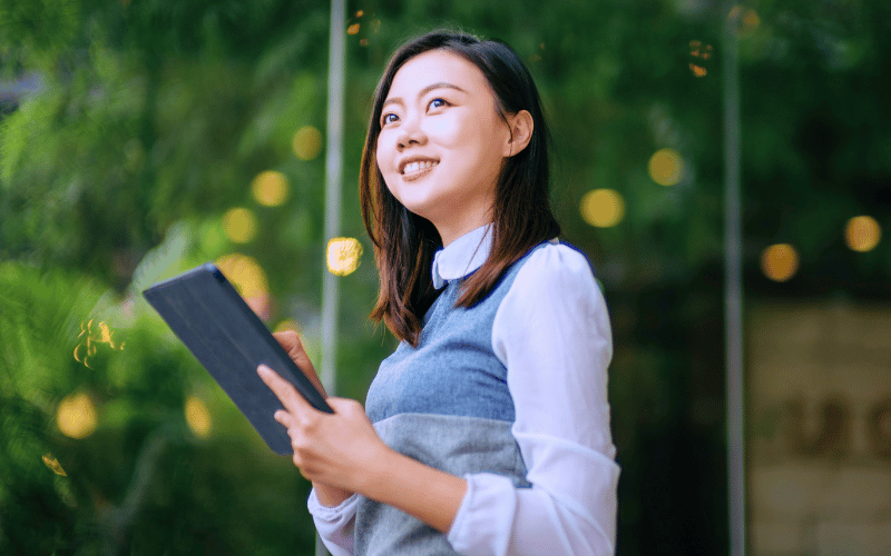 Woman holding a tablet outdoors, greenery background