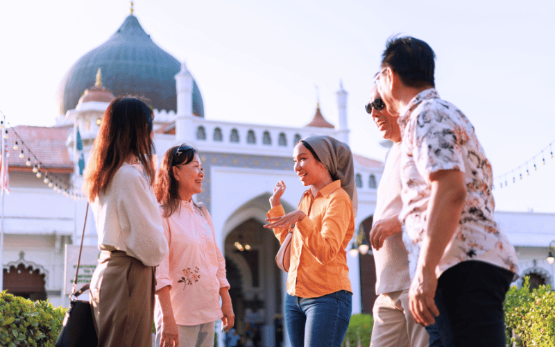 Group of young adults engaging in conversation outside a mosque, highlighting cultural heritage and community connection in a travel setting.