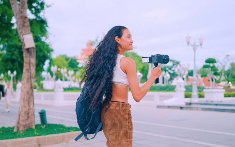 Young woman filming with a camera in an outdoor travel destination, promoting sustainable tourism.