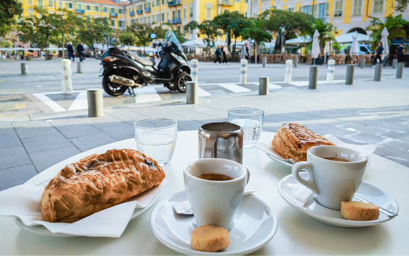 Two cups of coffee and pastries sitting on a café table overlooking Place Giuseppe Garibaldi in Nice, France