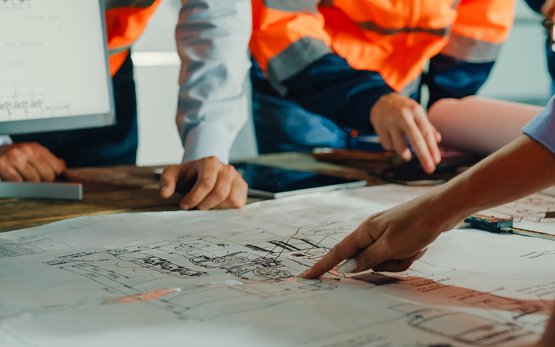 Closeup of team of industrial engineers meeting analyse machinery blueprints