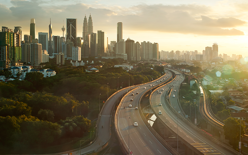 Warm sunset hues bathe a bustling city skyline and curving highway in golden light