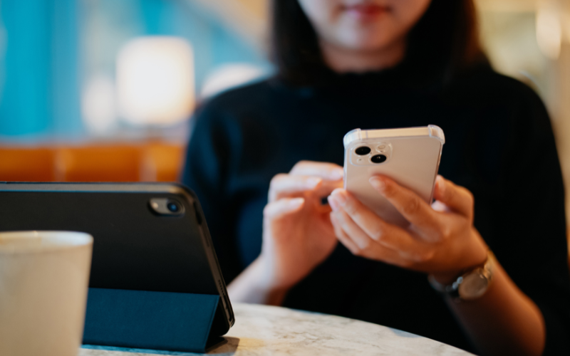 Woman using her iPhone while her iPad rests on the table