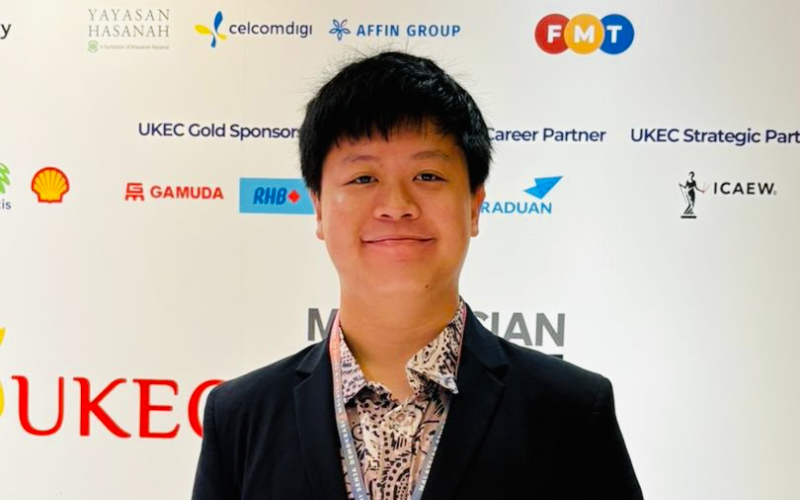 Joe Han standing in front of a sponsor-branded backdrop at a UKEC education event