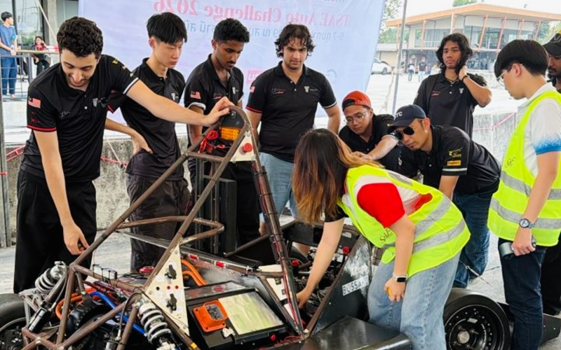 Members of Taylor's Racing Team working on the vehicle's chassis and wiring at a competition