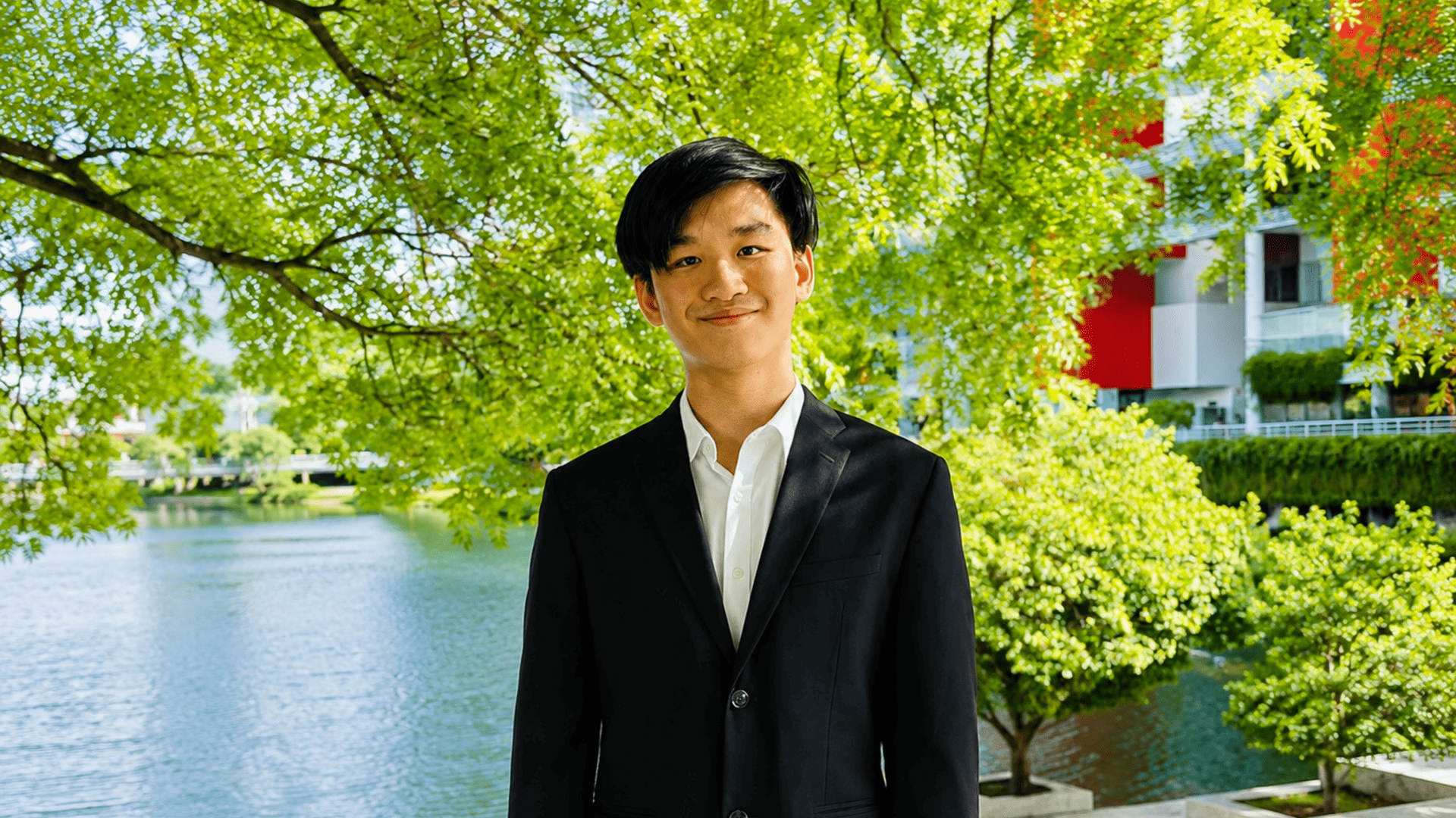 Portrait of Justin Khoo Jon Le smiling outdoors on Taylor's campus, with a lake and greenery in the background.