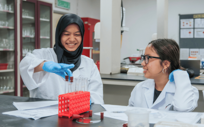 Two students conducting a laboratory experiment while smiling and interacting in a science lab.