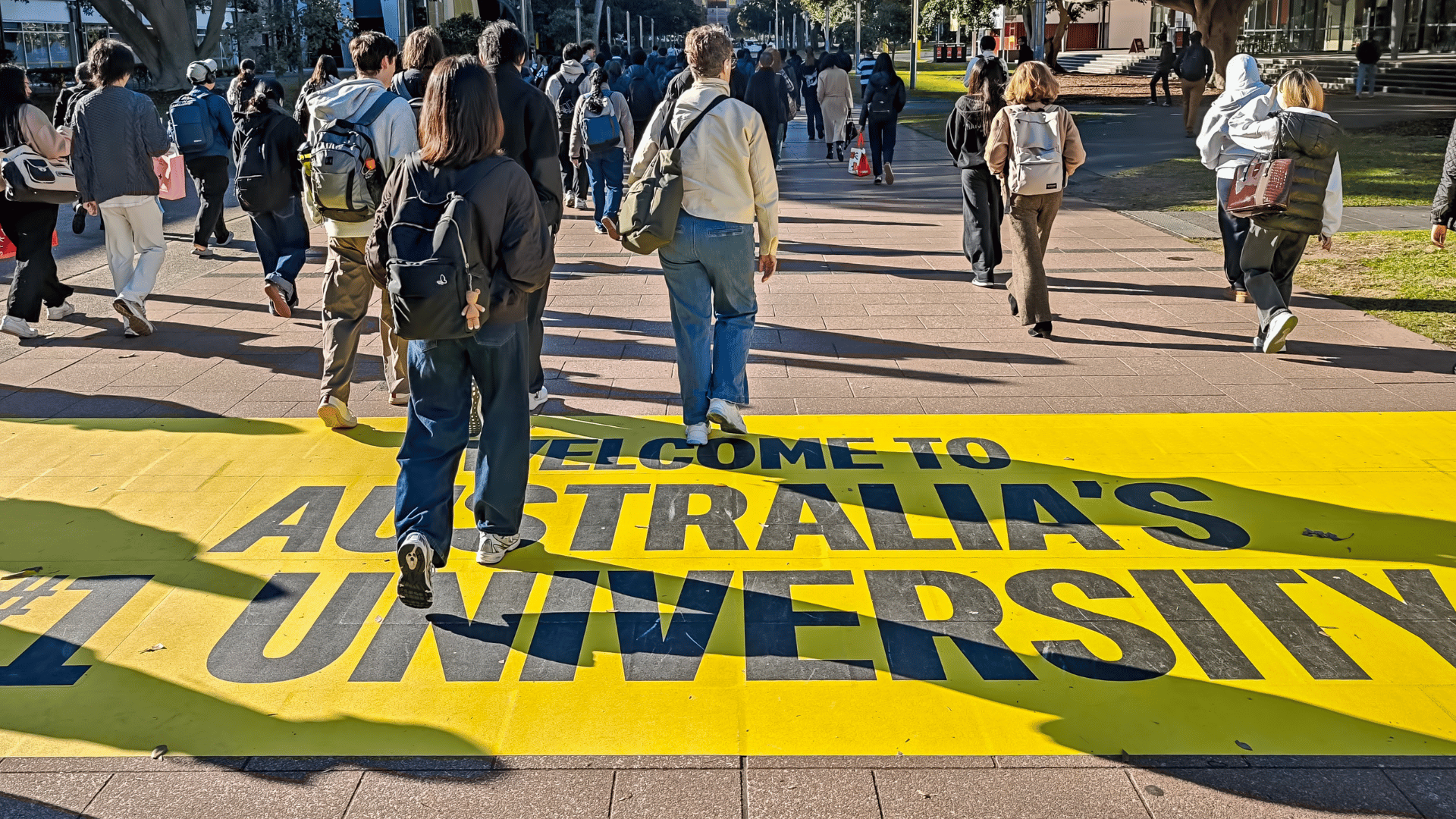 People walking across a yellow walkway with the words "YOUR 1ST AUSTRALIAN UNIVERSITY".