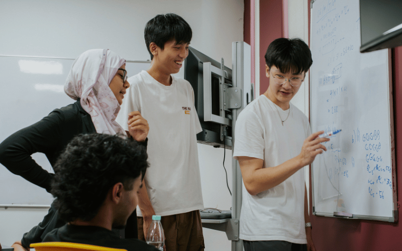 Engineering students discussing ideas around a whiteboard in a classroom