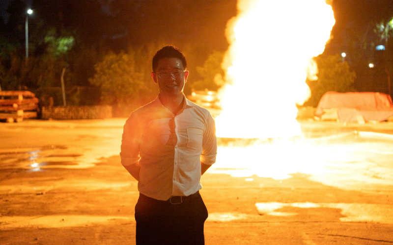 Brian Soo standing in front of a large controlled fire at night at an outdoor training ground
