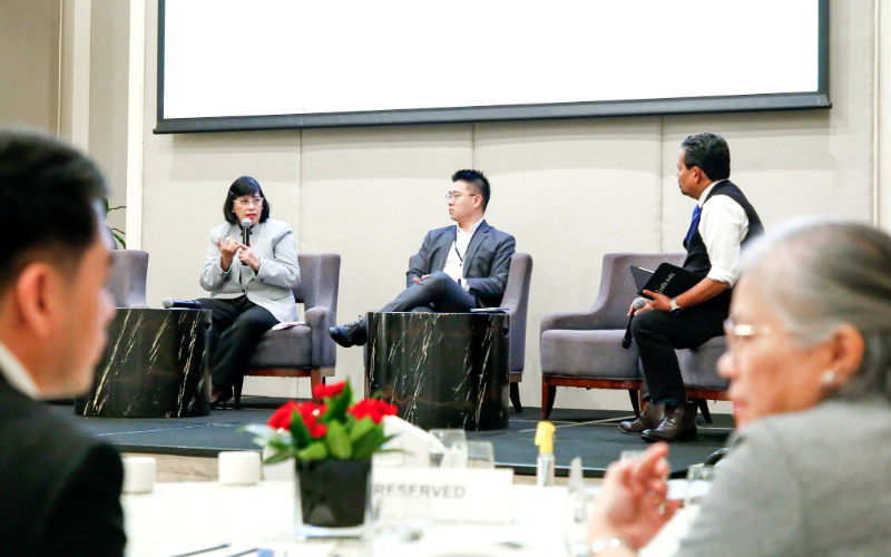Brian Soo speaking as a panellist on stage beside two other speakers at a business forum