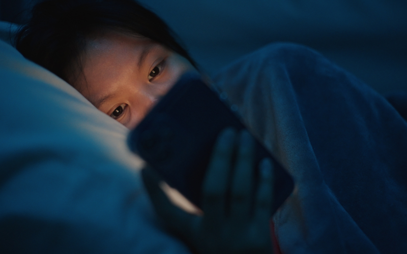 A girl lying in bed at night, using a smartphone