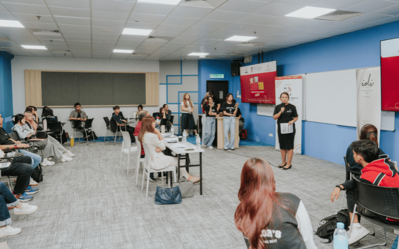 A presenter speaking to an audience seated in a classroom in The Real Tea event